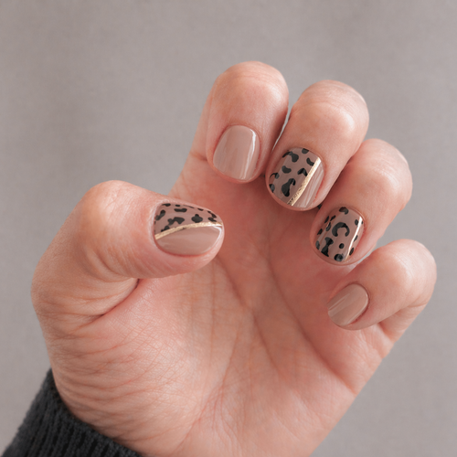 Hand with nails painted in a pattern of dots and stripes on a neutral background