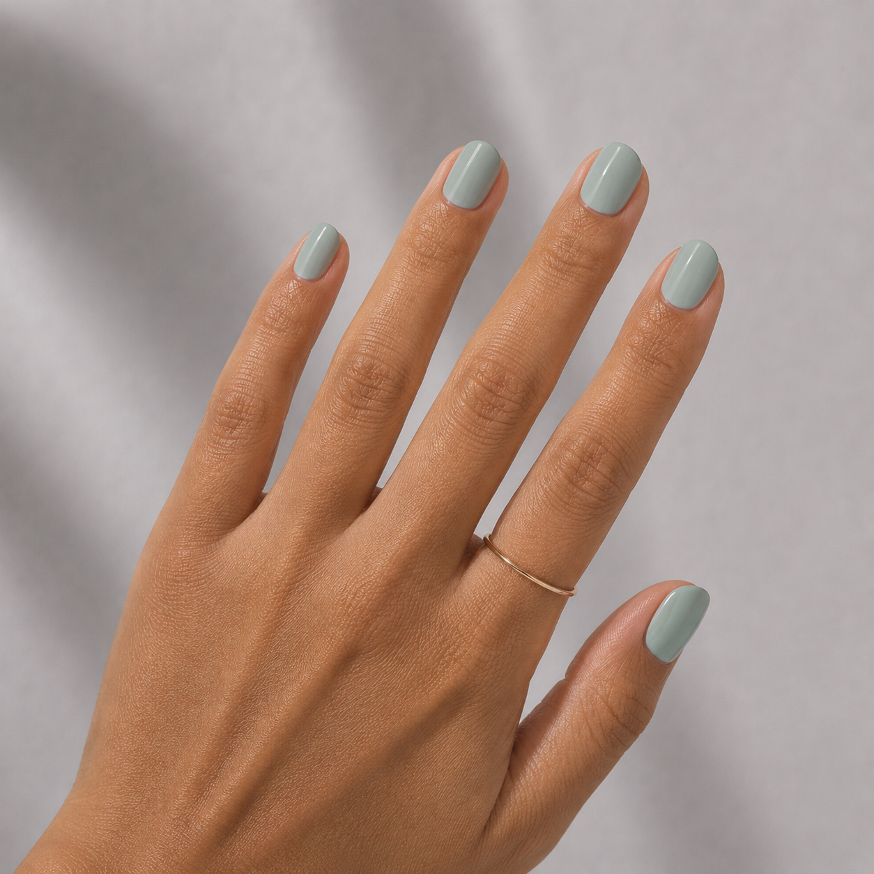 Hand with light green nail polish on a neutral background