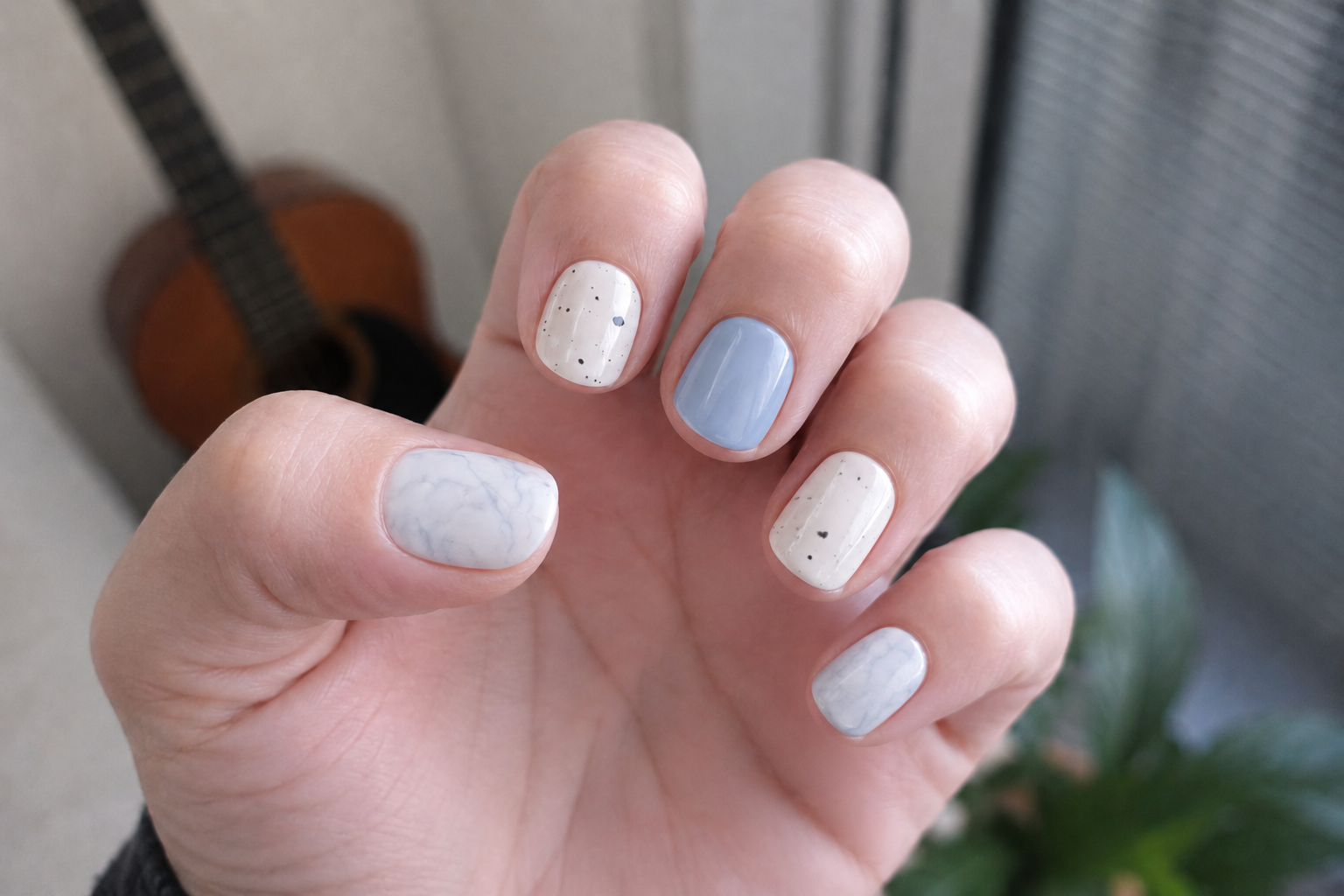 Hand with light blue and beige nail polish against a blurred indoor background